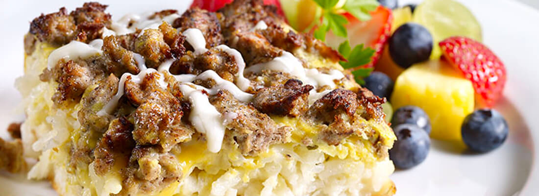 A breakfast casserole of potato hash, cheese and ground turkey with a side of mixed fruit.