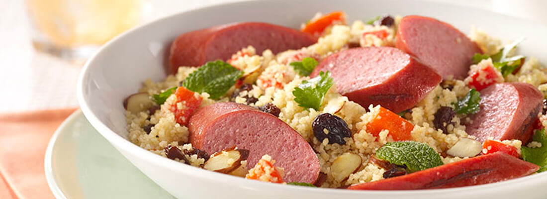 A plateful of sliced sausage, quinoa, herbs, nuts and diced vegetables.
