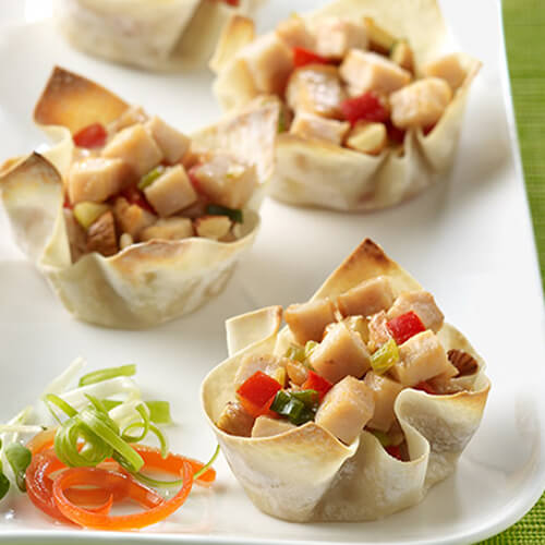 Wonton cups filled with turkey, veggies, and almonds on a white platter with a green background.