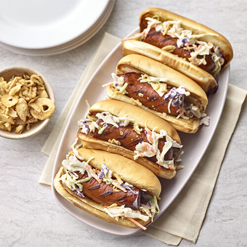 A flavorful hoagie loaded with andouille sausage loaded with pepper, paprika and garlic, and layers on fresh coleslaw and crispy fried onions. served on a white platter.