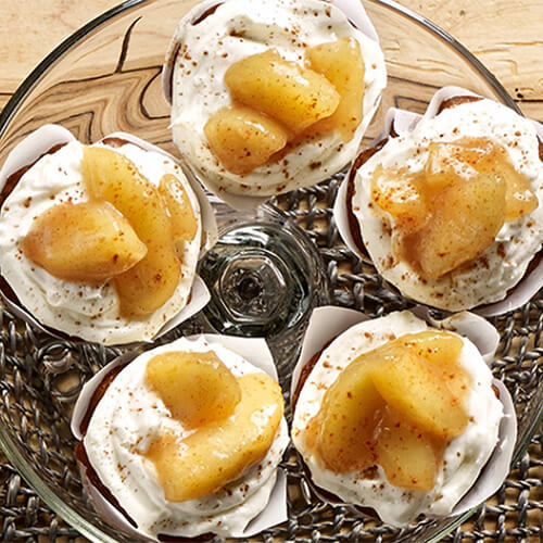 A carrot cupcake made with fresh cream cheese frosting and cinnamon apples, served on a glass tray