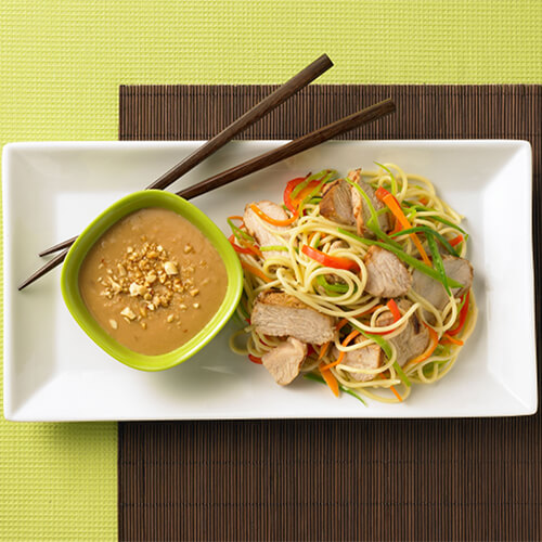 Asian noodle turkey salad with a side of peanut sauce on a white plate with chopsticks.