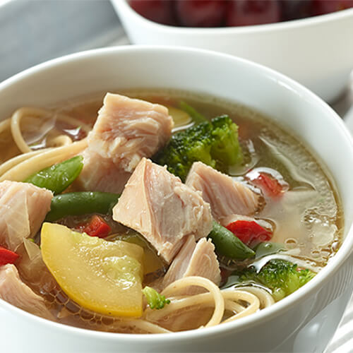 A noodle soup packed with veggies, lean turkey and savory Asian flavors, served in a white bowl.