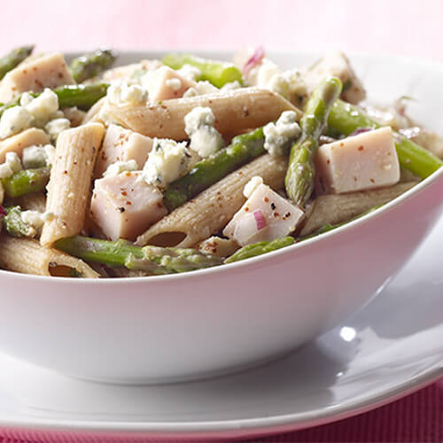 Fresh spring pasta filled with steamed asparagus, lean cubed turkey, and crumbled blue cheese, served in a white bowl on a pink tablecloth.