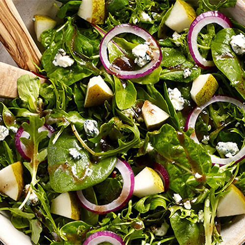 An eclectic mix of salad greens, red onion, blue cheese, pears and balsamic vinaigrette, served in a wooden bowl.