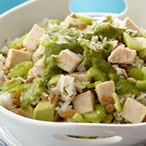 Tangy green chilies, cilantro and avocado combined with sunflower seeds, golden raisins, and lean turkey, served in a white bowl on a porcelain platter.