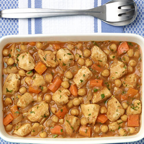 Baked turkey tenderloins made with onions, carrots, and garlic, served with a lemon, herb, and tomato sauce, served in a light blue baking dish on a navy and white patterned tablecloth.