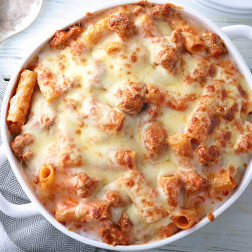 A hearty bake made of rigatoni pasta, turkey, provolone cheese, and spaghetti sauce. served in a white bowl atop a wooden table.