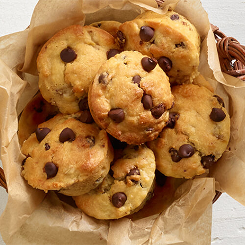 Rich, indulgent muffins made with chocolate and bananas, served on parchment paper in a wood woven bowl, atop a wooden table.