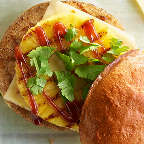 Barbeque pineapple turkey burger garnished with cilantro on a white plate.