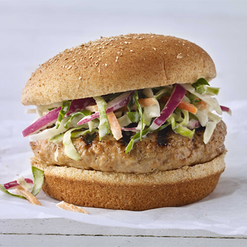 Barbeque turkey burgers with coleslaw falling out in a white table.