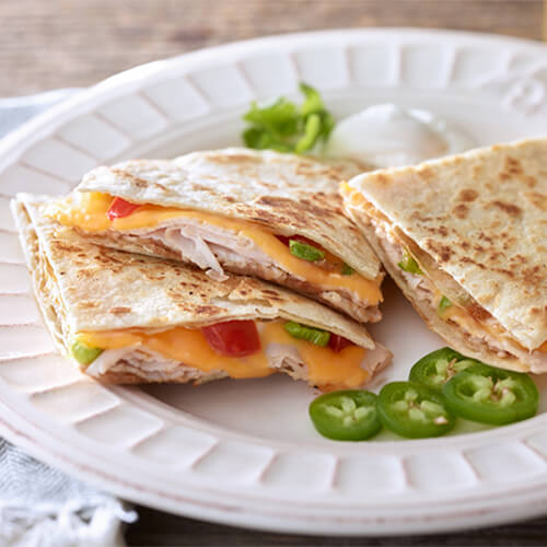 Simple quesadillas made from refried beans, scallions, peppers, and turkey, served with a side of sour cream and garnished with jalapeno, served on a white plate.