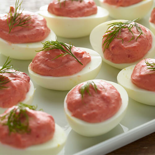 Beet deviled eggs garnished with a sprig of dill on a white tray