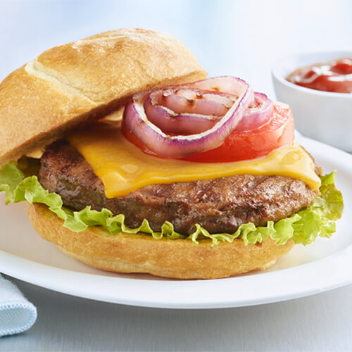 A turkey burger topped with grilled onion, tomato and lettuce, served on a white plate.