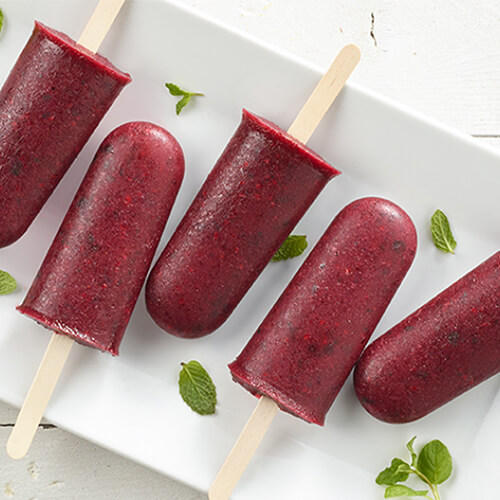 Delicious popsicles made with fresh blackberries, sugar, and mint leaves, served on a white plate atop a wooden table.