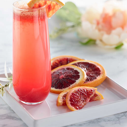 Blood orange spritzer garnished with sliced blood orange on a white tray.