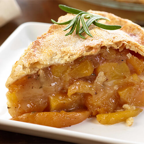 Bourbon peach pie garnished with rosemary on a white plate.