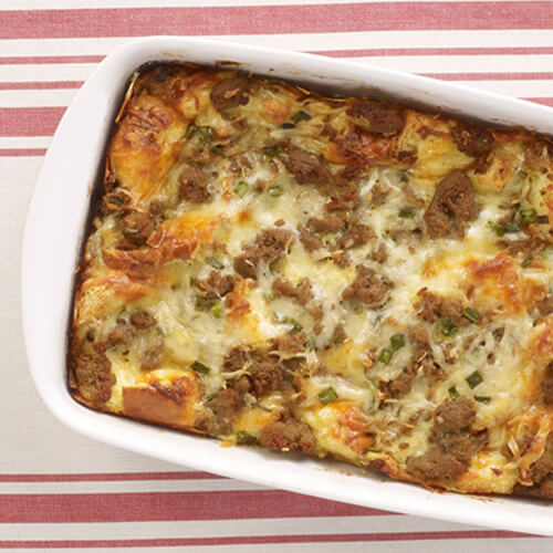 Breakfast strata casserole with turkey sausage in a white baking dish on a red striped tablecloth.