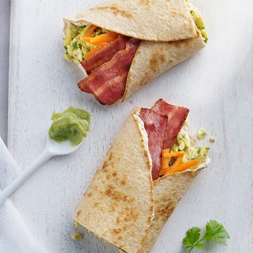 A healthy breakfast rollup filled with crispy turkey bacon, fresh cilantro, crunchy carrots and fluffy eggs served on a small white spoon and a white platter.