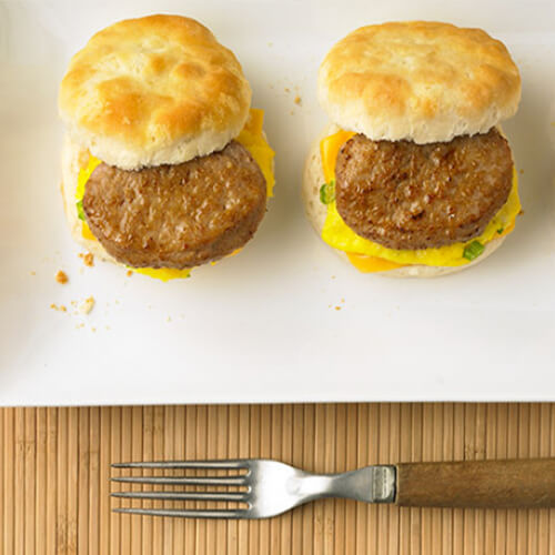 3 delicious biscuits topped with turkey sausage, eggs and cheese on a white platter, on a wooden placemat on a blue tablecloth.