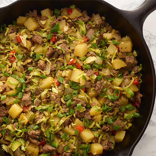 Brussel sprout turkey sausage and potato hash garnished with green onions in a cast iron skillet.