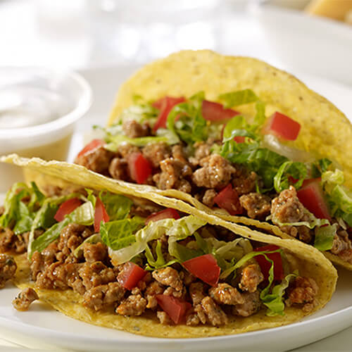 Flavorful tacos made with spicy turkey and fresh vegetables, served with a side of ranch dressing on a white plate.