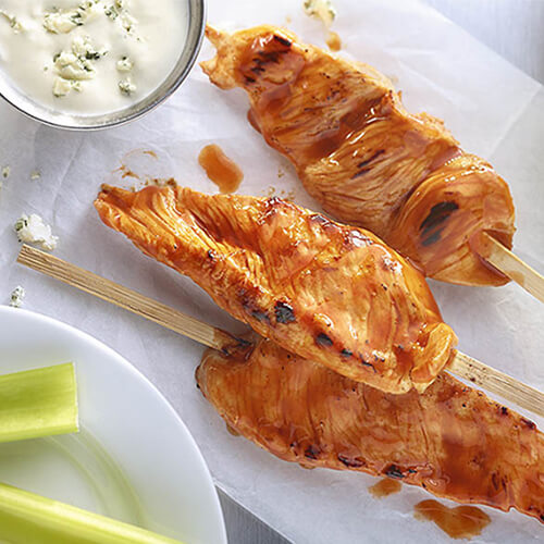 Skewered turkey tenderloin marinated in a spicy onion and garlic mix, served with a blue cheese buffalo sauce, on parchment paper.