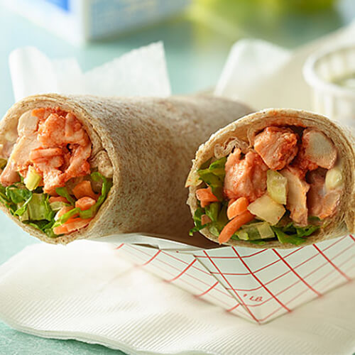 A wrap filled with turkey, Buffalo sauce, and veggies, served with a blue cheese dressing in a paper bowl.