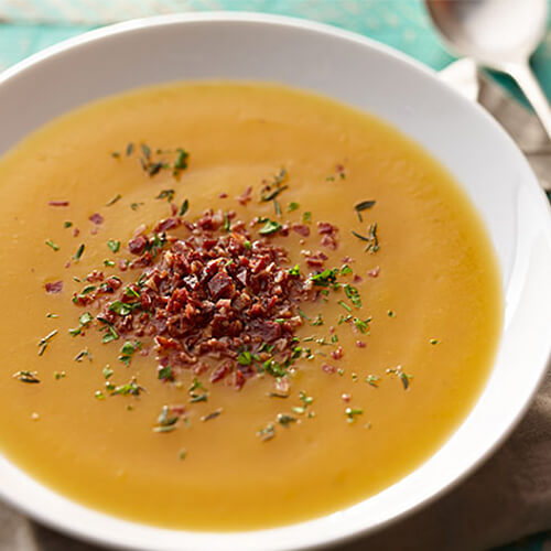 Butternut squash and apple soup garnished with spices in a white bowl.