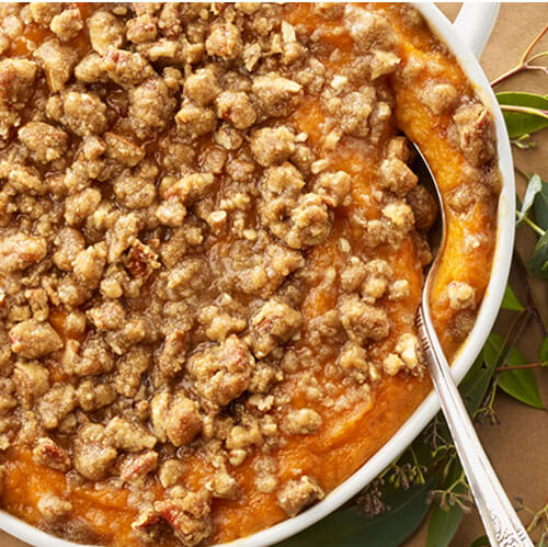 Butternut squash and sweet potato casserole in a white dish with a spoon.