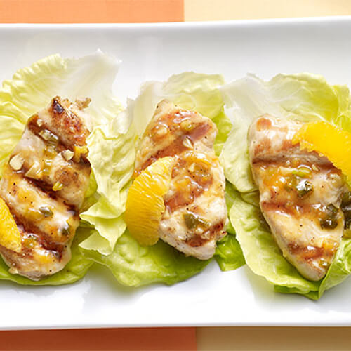 Turkey tenderloin made with orange wedges and nestled in lettuce leaves on a white tray.
