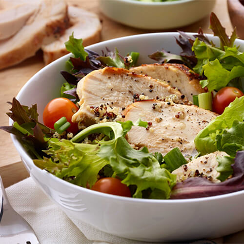 Cajun turkey and quinoa salad bowl garnished with tomatoes in a white bowl.