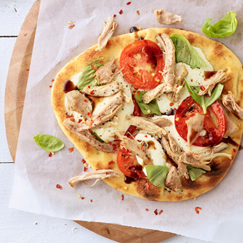 Caprese turkey flatbread garnished with basil on a wood plate.