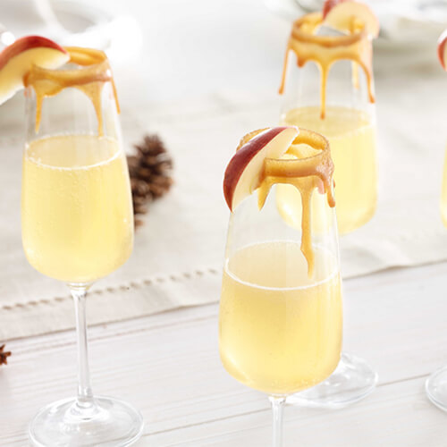 Caramel apple mimosa garnished with an apple slice on a white wood table.