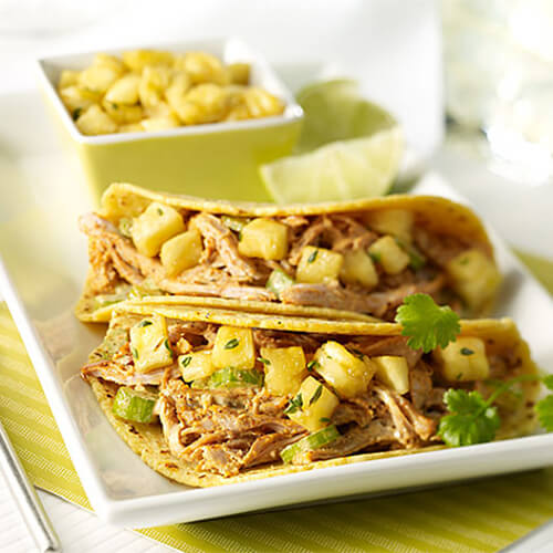 Turkey made with Caribbean Jerk spices, topped with pineapple salsa inside tortilla shells, garnished with cilantro on a white platter atop a green cloth.