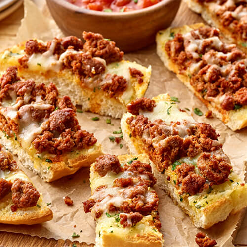 Delicious garlic bread topped with bold chorizo flavor, served with with fresh salsa and jalapeno slices on parchment paper on a wooden board.