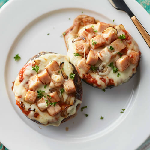 Two large mushroom caps topped with tomato sauce, Monterey jack cheese and chunk of turkey meat.