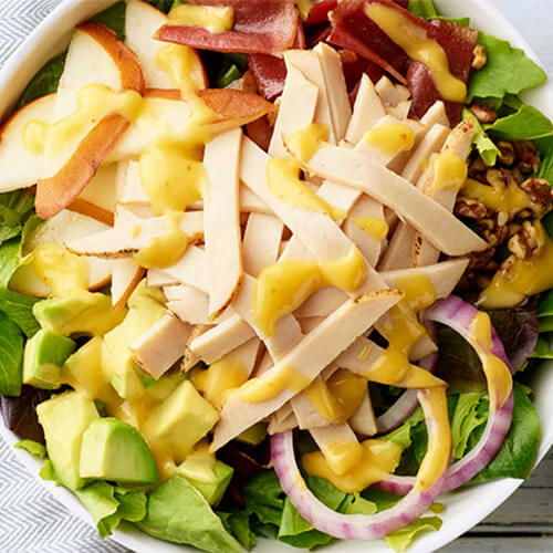 Chicken pear and avocado salad drizzled with dressing in a grey bowl.