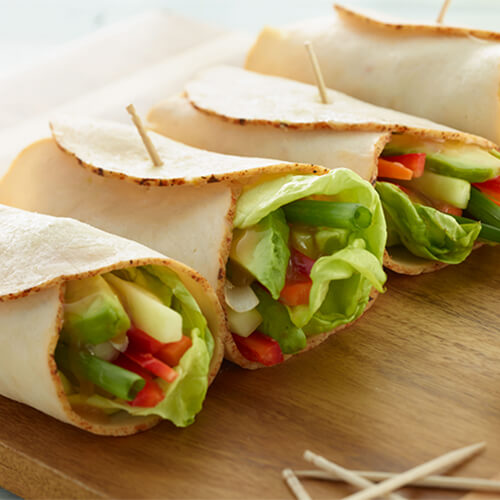 Chicken vegetable wrap held together with toothpicks on a wood cutting board.