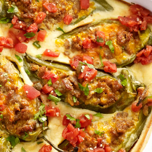 Blackened chilies, turkey sausage, cheese, veggies, and egg, served in a white casserole tray atop a light gray tablecloth.