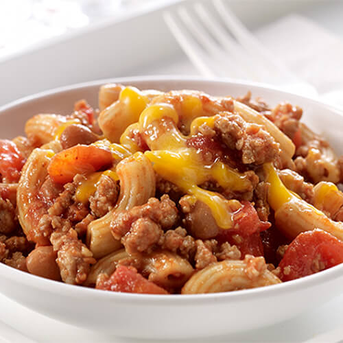 Macaroni combined with ground turkey, tomatoes, pinto beans and taco seasoning, served in a white bowl on a white plate.