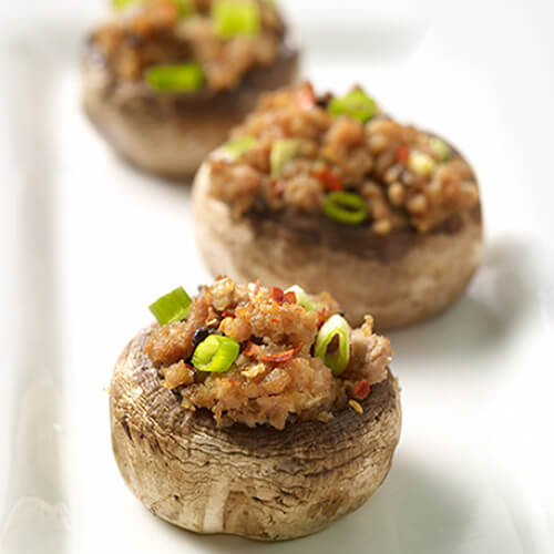 Turkey stuffed mushrooms topped with ginger root, breadcrumbs, red pepper flakes and green onions, on a white platter with a green placemat and red chopsticks.