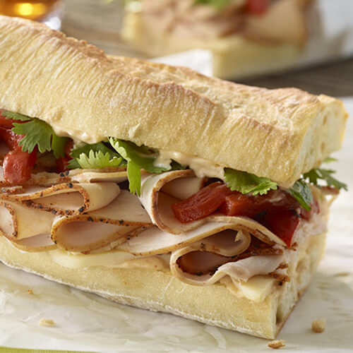 A sandwich filled with melted Monterey jack, cajun-style turkey, and vegetables, topped with chipotle mayo, served on parchment paper.