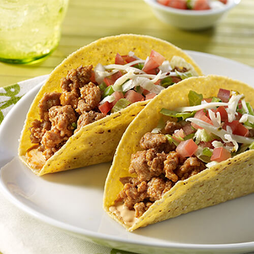 Turkey tacos with fresh veggies and homemade pico de gallo, served on a white plate atop a green patterned cloth.