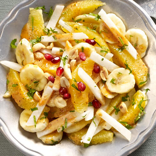 Bananas, orange sections, and jicama, made into a salad, served on a light gray plate on a dark gray tablecloth.