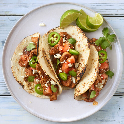 Sauteed peppers, tomatoes, lean turkey, and cheese all in crispy tortillas served on a gray plate garnished with limes and cilantro.