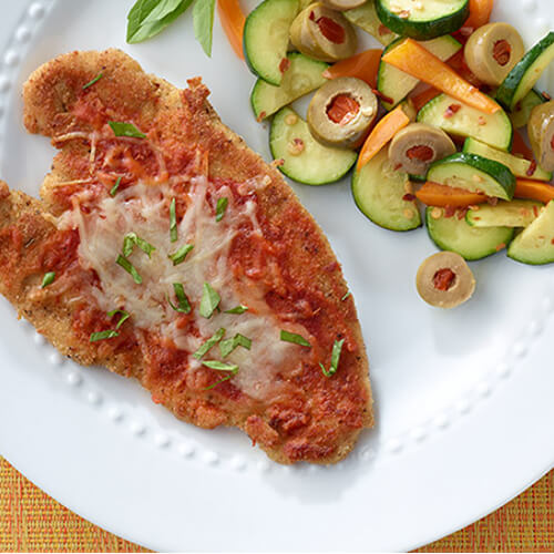 A meaty piece of turkey breast topped with tomato sauce, parmesan cheese and basil next to a side vegetables.