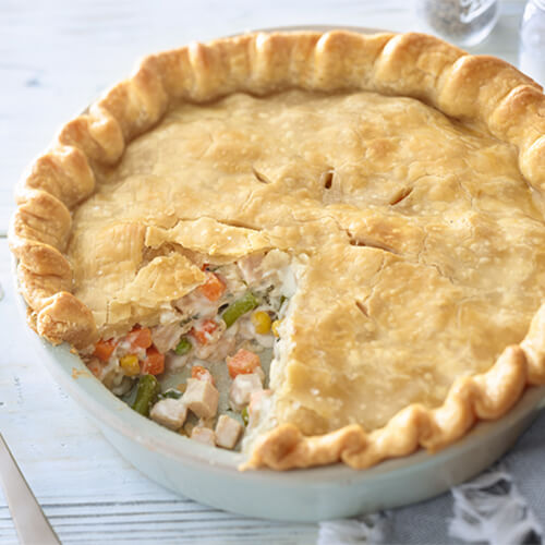 A pie with a flaky crust, filled with JENNIE-O® turkey, carrots, and peas in a white baking dish.