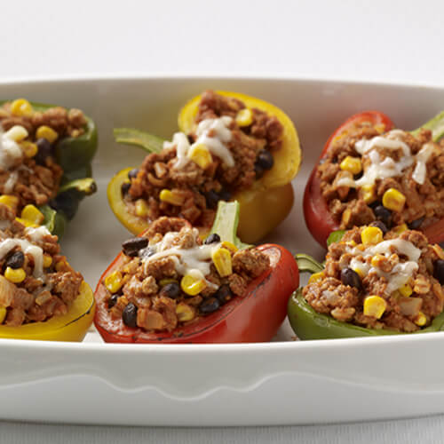 Colorful peppers stuffed with lean ground turkey, beans, cheese and flavorful veggies, served in a white tray.