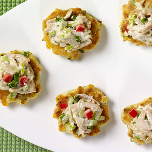 Crispy corn cake fritters topped with a delicious portion of turkey salad, served on a white platter, atop a green woven tablecloth.